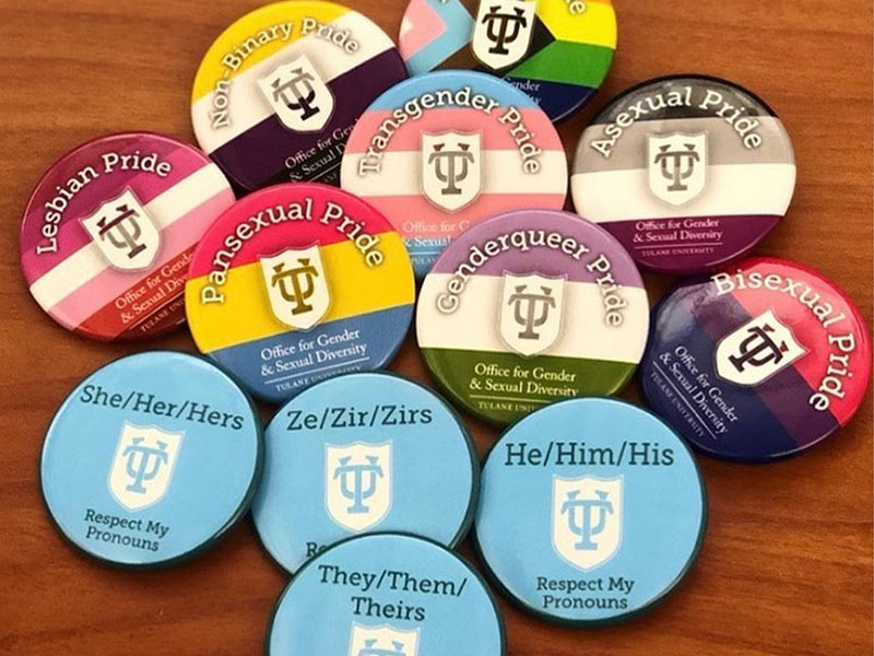 Pile of "My Pronouns Are"buttons on a wooden table.